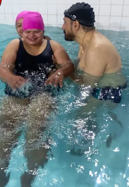 Participante de touca rosa sendo apoiada por um professor na piscina