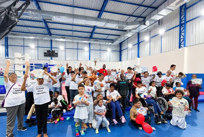 Todos juntos no ginásio azul: alunos, familiares e professores, alguns em cadeira de rodas, com certificados e balões