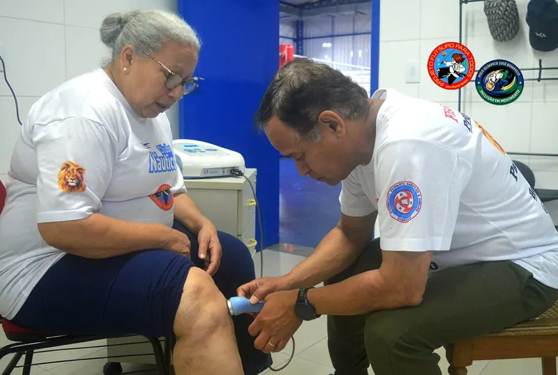 Atendimento de fisioterapia: professor aplicando aparelho no joelho de uma aluna sentada